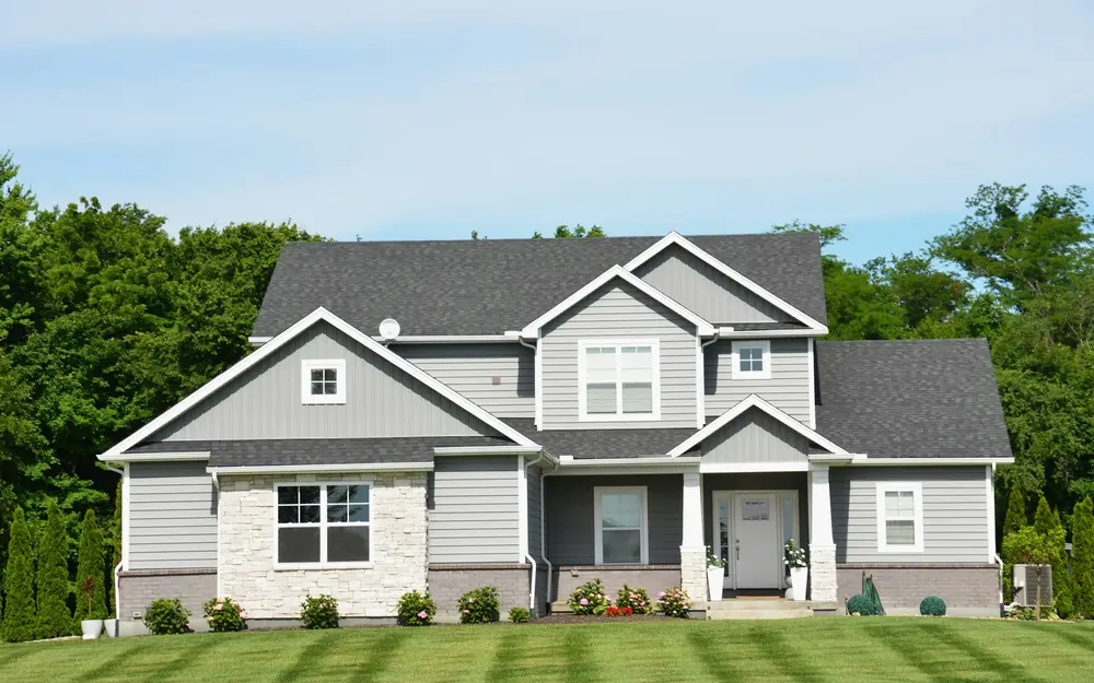 A gray family home with multiple shingle roof planes, white gable trim and a green lawn.