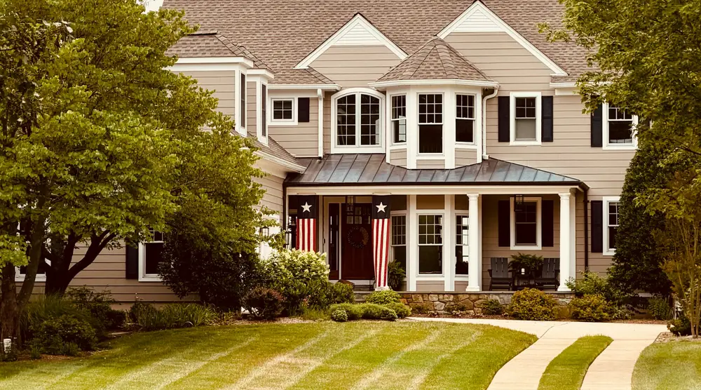 A two-story home with a broad front porch, pitched roof and neatly mowed lawn.