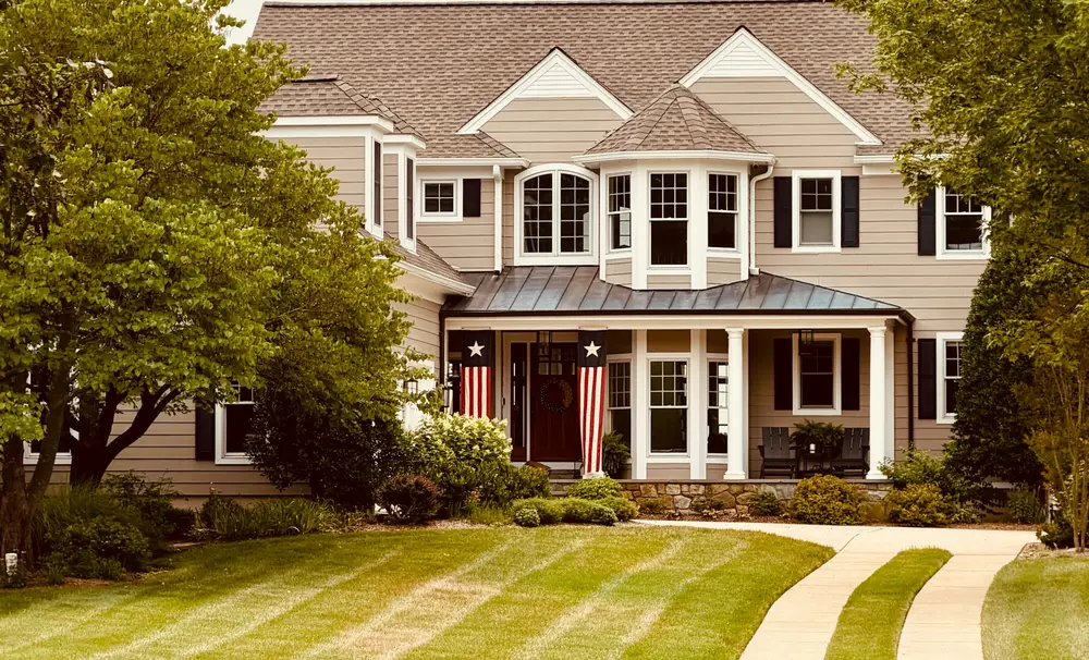A two-story home with a broad front porch, pitched roof and neatly mowed lawn.