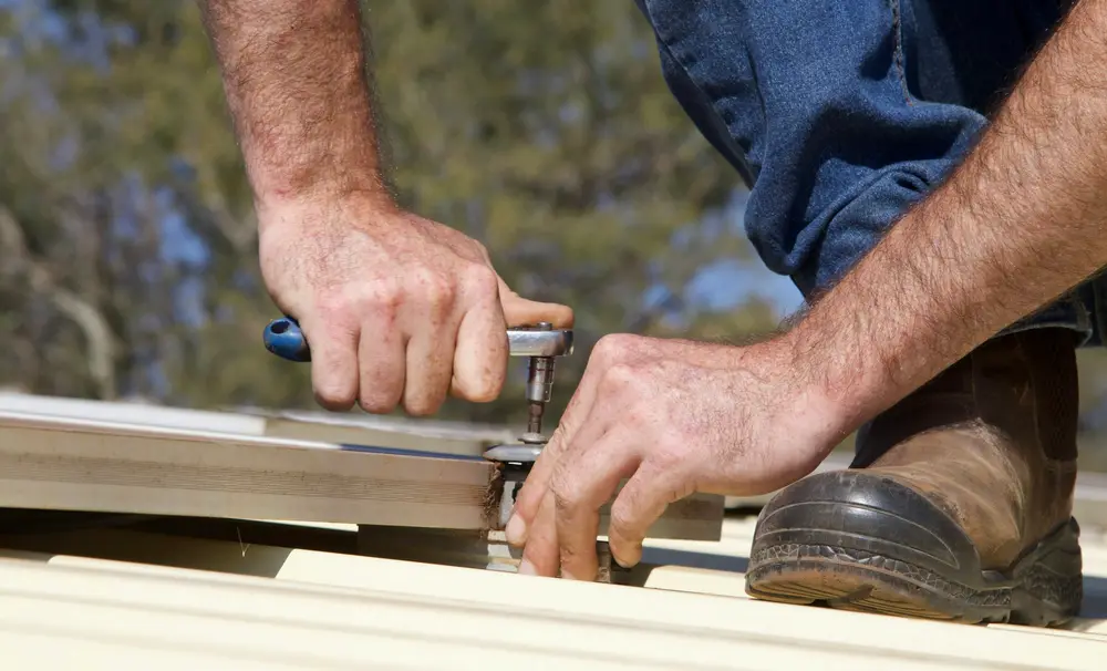 Close view of a worker fastening a metal panel at the roof edge.